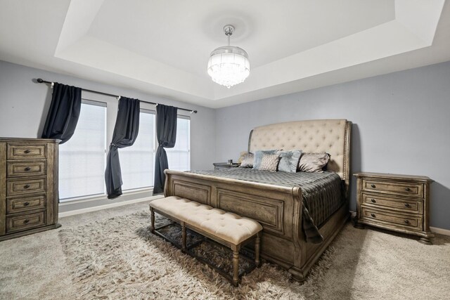 carpeted bedroom featuring a notable chandelier and a raised ceiling