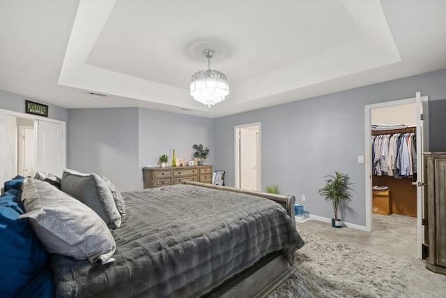 bedroom with a tray ceiling, carpet, a spacious closet, and a chandelier