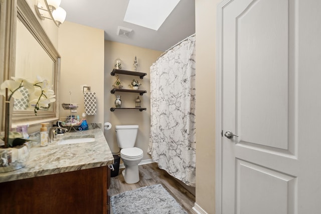 bathroom featuring wood-type flooring, a skylight, vanity, and toilet