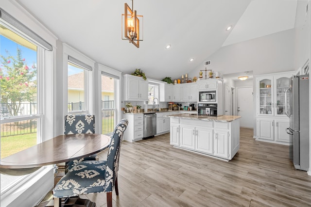 kitchen with light wood-type flooring, a kitchen island, white cabinetry, appliances with stainless steel finishes, and light stone counters