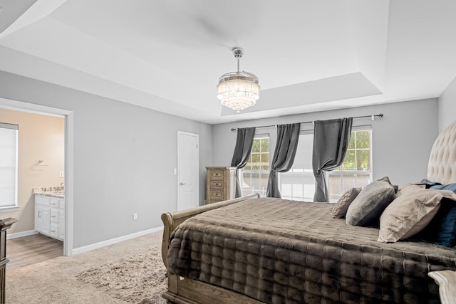 bedroom with a raised ceiling, an inviting chandelier, connected bathroom, and wood-type flooring