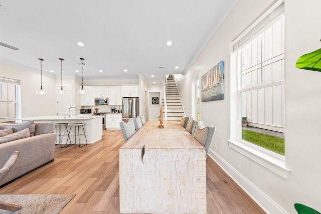 kitchen featuring light hardwood / wood-style flooring, white cabinets, an island with sink, appliances with stainless steel finishes, and a kitchen bar