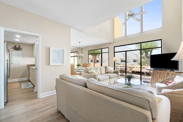 living room with light hardwood / wood-style floors, ceiling fan with notable chandelier, and a textured ceiling