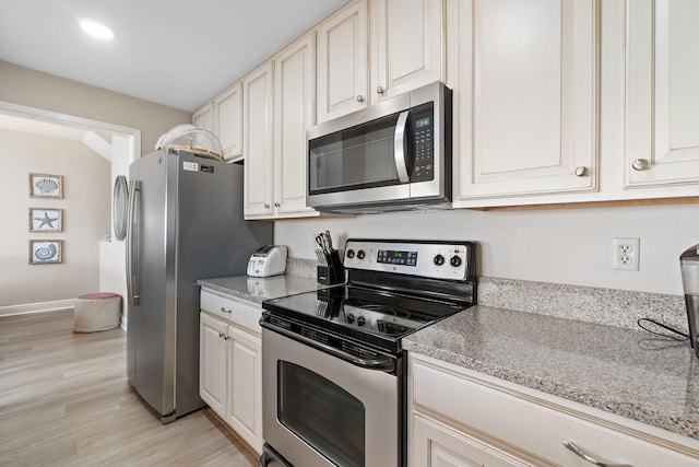 kitchen with light stone counters, appliances with stainless steel finishes, and light hardwood / wood-style flooring