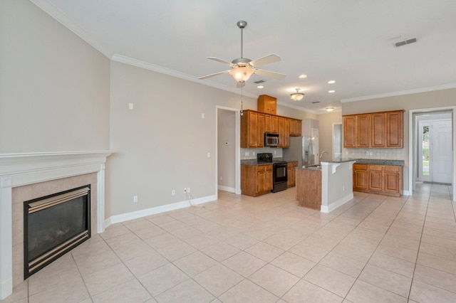 kitchen with stainless steel appliances, a fireplace, light tile patterned floors, a kitchen island with sink, and ceiling fan