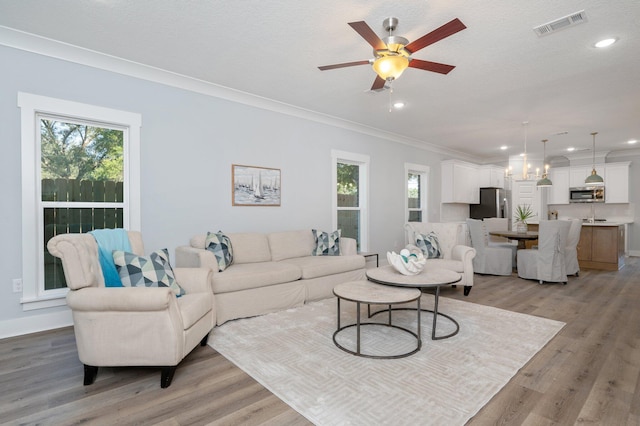 living area with ornamental molding, light wood-type flooring, visible vents, and recessed lighting