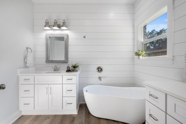 bathroom with a freestanding tub, baseboards, wood finished floors, and vanity