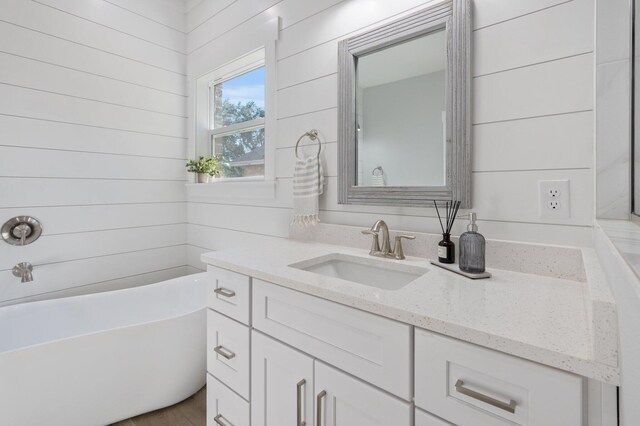 bathroom with wooden walls, a freestanding tub, and vanity