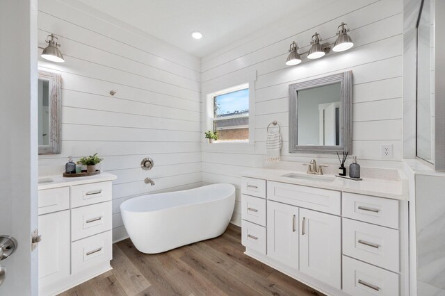 full bath featuring wood finished floors, a freestanding tub, two vanities, and a sink