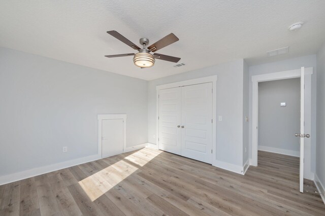 unfurnished bedroom with a closet, visible vents, a ceiling fan, wood finished floors, and baseboards