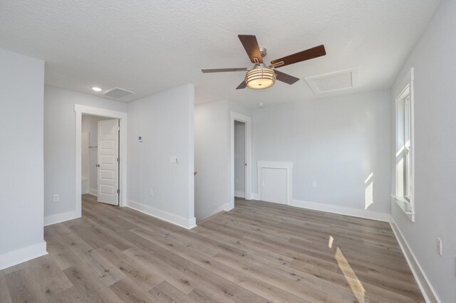 spare room featuring attic access, baseboards, light wood-style flooring, and a textured ceiling