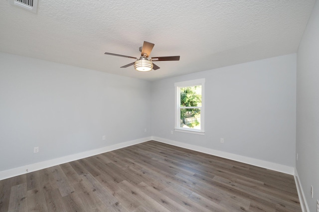 empty room with a textured ceiling, wood finished floors, visible vents, and baseboards