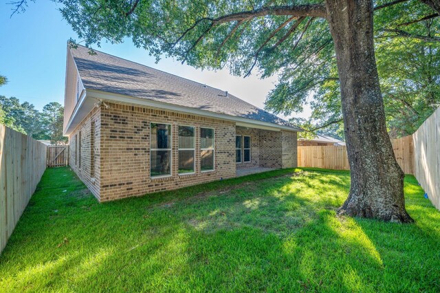 back of property featuring a yard, a fenced backyard, a shingled roof, and brick siding