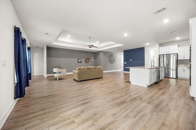 unfurnished living room featuring sink, light wood-type flooring, ceiling fan, and a raised ceiling