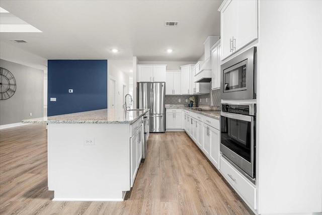 kitchen with a kitchen island with sink, light hardwood / wood-style flooring, stainless steel appliances, and backsplash