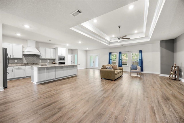 living room featuring ceiling fan, sink, light wood-type flooring, and a tray ceiling