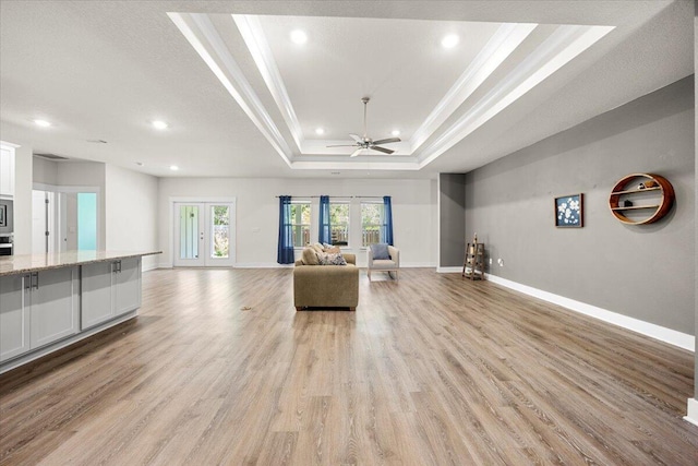 unfurnished living room with ceiling fan, french doors, a tray ceiling, and light hardwood / wood-style floors