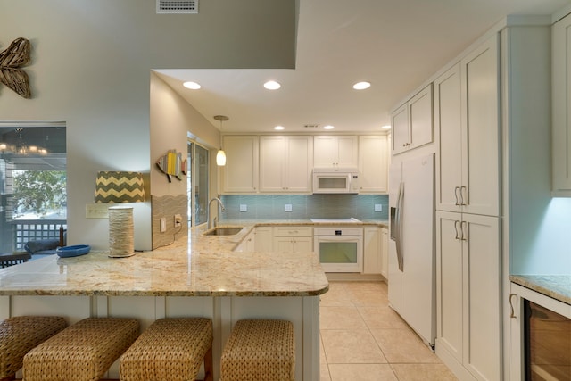 kitchen featuring a kitchen bar, white appliances, sink, kitchen peninsula, and hanging light fixtures