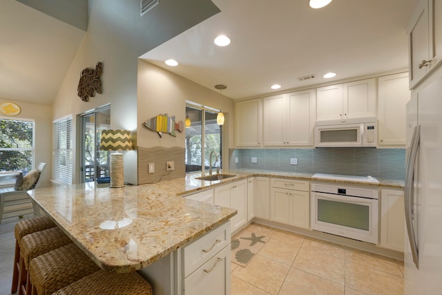 kitchen with a breakfast bar area, white appliances, light tile patterned floors, kitchen peninsula, and sink