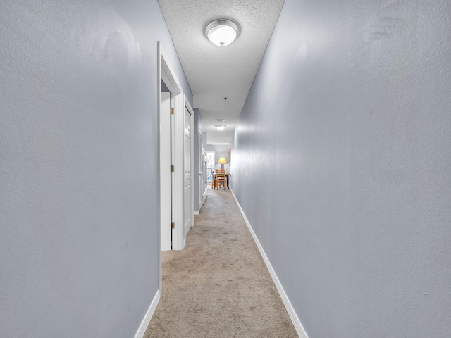 corridor with light carpet, baseboards, and a textured ceiling