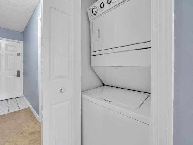 laundry room with light carpet, laundry area, light tile patterned floors, stacked washer and clothes dryer, and a textured ceiling