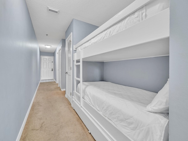 bedroom with baseboards, visible vents, a textured ceiling, and light colored carpet