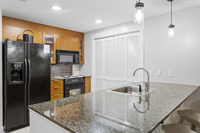 kitchen with a breakfast bar, sink, dark stone countertops, pendant lighting, and black appliances