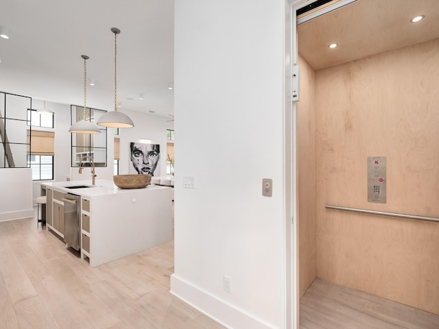 kitchen with elevator, light wood-type flooring, a center island with sink, decorative light fixtures, and sink