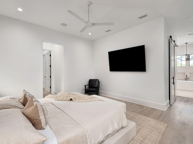 bedroom with ceiling fan, ensuite bathroom, light wood-type flooring, and a barn door