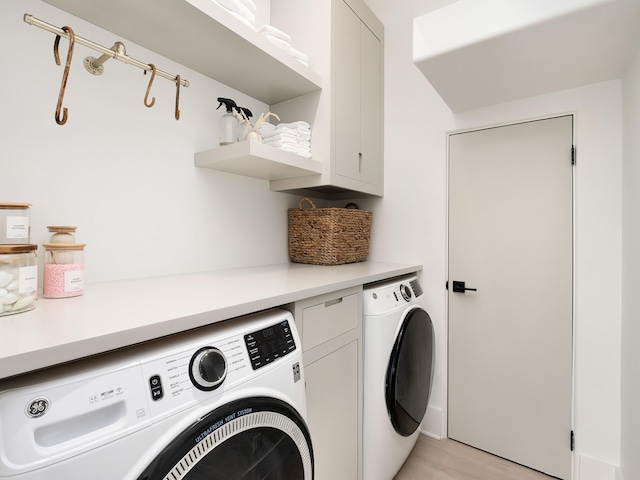 laundry room featuring washer and clothes dryer, cabinets, and light hardwood / wood-style flooring