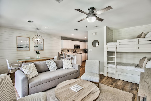 living room with wooden walls, ceiling fan with notable chandelier, and dark hardwood / wood-style floors