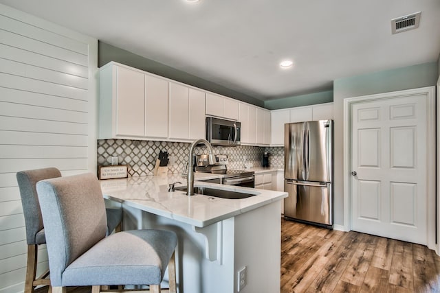 kitchen featuring tasteful backsplash, stainless steel appliances, white cabinets, light wood-type flooring, and kitchen peninsula