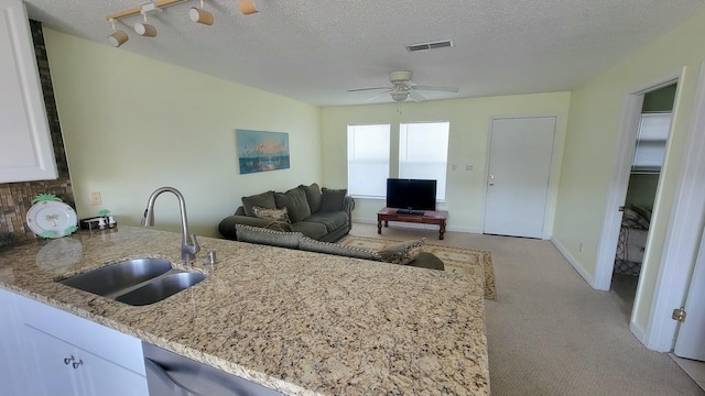 interior space with visible vents, ceiling fan, white cabinetry, light stone counters, and a sink