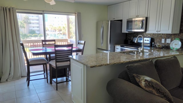 kitchen featuring light stone countertops, appliances with stainless steel finishes, a peninsula, light tile patterned floors, and tasteful backsplash