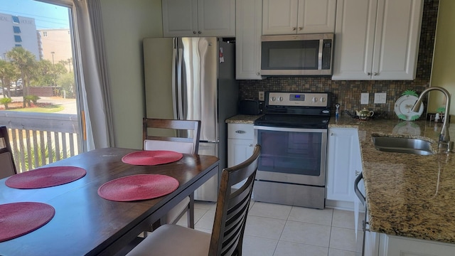 kitchen with light tile patterned flooring, appliances with stainless steel finishes, a sink, stone countertops, and decorative backsplash