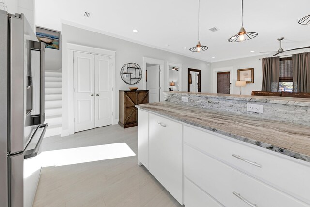 kitchen with decorative light fixtures, white cabinets, crown molding, stainless steel refrigerator with ice dispenser, and light stone countertops