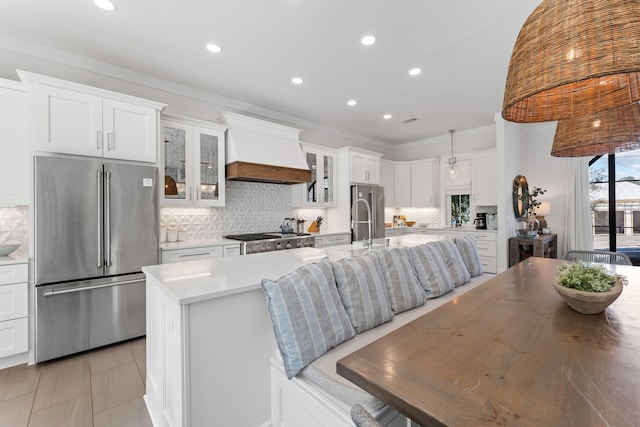 kitchen featuring stainless steel fridge, custom range hood, white cabinets, an island with sink, and high end refrigerator