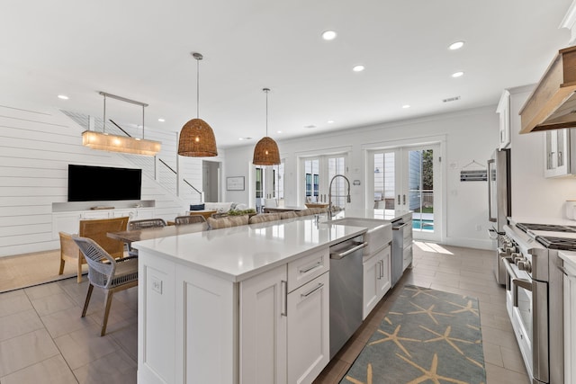 kitchen featuring stainless steel appliances, hanging light fixtures, white cabinets, sink, and a center island with sink