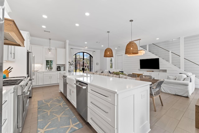 kitchen with white cabinetry, tile patterned floors, decorative light fixtures, an island with sink, and appliances with stainless steel finishes