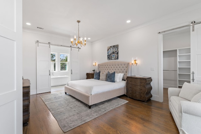 bedroom featuring a walk in closet, ornamental molding, a barn door, and dark hardwood / wood-style flooring