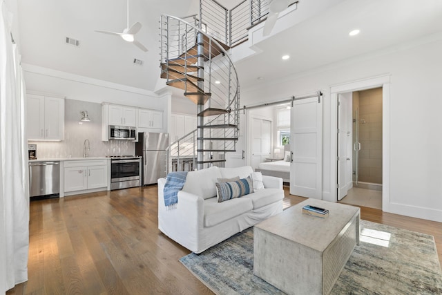 living room with hardwood / wood-style floors, sink, a barn door, ceiling fan, and a towering ceiling