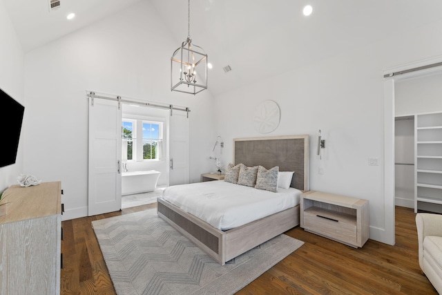 bedroom featuring dark wood-type flooring, a barn door, high vaulted ceiling, and a walk in closet