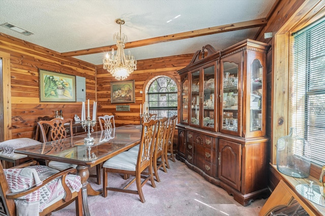 dining room featuring a notable chandelier, beamed ceiling, wood walls, carpet, and a textured ceiling