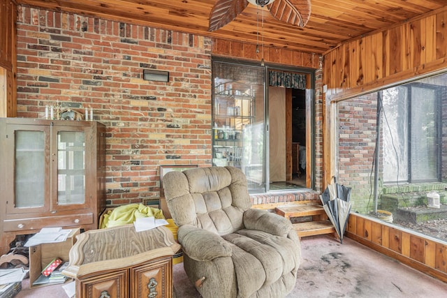 sitting room featuring ceiling fan, brick wall, and wooden ceiling