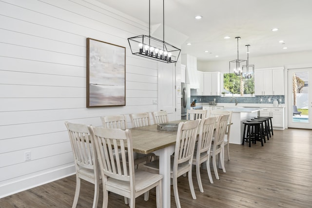 dining area with recessed lighting, a notable chandelier, dark wood finished floors, and wooden walls