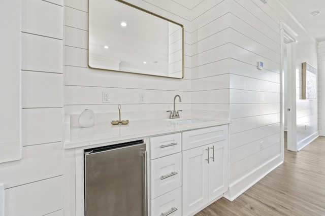 bar featuring a sink, light wood-type flooring, and stainless steel fridge