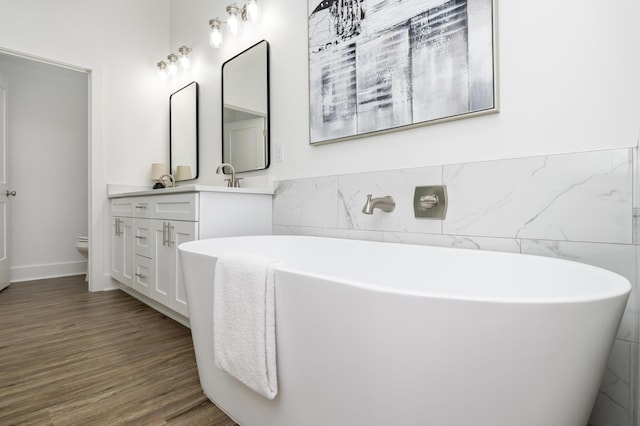 full bathroom with toilet, wood finished floors, vanity, tile walls, and a freestanding bath