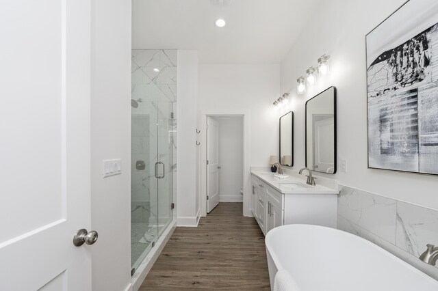 bathroom with a sink, wood finished floors, a soaking tub, a shower stall, and double vanity