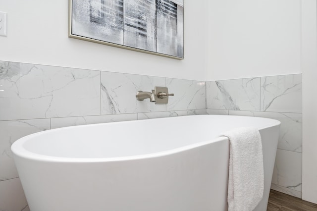 bathroom featuring wood finished floors, a freestanding tub, and tile walls