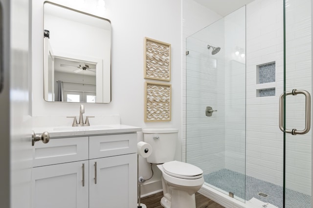 full bath featuring toilet, vanity, wood finished floors, tiled shower, and baseboards